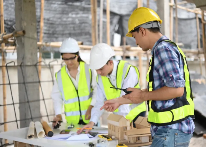 drei Menschen mit Helmen und Warnweste über Plan von Baustelle